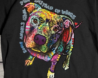 Può includere: T-shirt nero con grafica colorata di un cane e la scritta "Some Angels Have Fur Instead of Wings". L'illustrazione del cane è vivace, con un mix di colori e motivi. La maglietta è in materiale morbido.