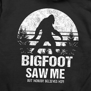 May include: Black hooded sweatshirt with a white graphic of Bigfoot walking in a forest with the text "Bigfoot Saw Me But Nobody Believes Him".