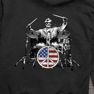 May include: Black hooded sweatshirt with a small American flag on the left chest and a graphic of a skeleton playing drums with an American flag peace sign on the back.