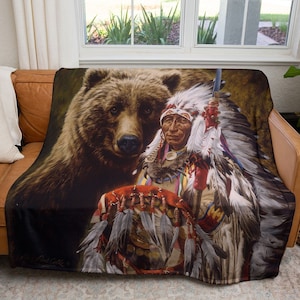 May include: A brown bear with a Native American chief in a headdress and feathers holding a drum. The chief is wearing a colorful beaded vest and a red and white headdress. The bear is looking at the viewer.