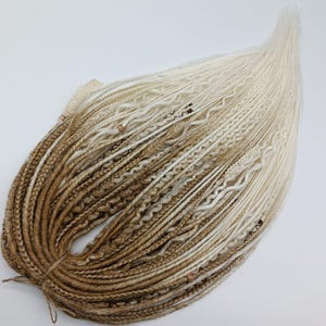 May include: A bundle of synthetic dreadlocks in a gradient of colors, transitioning from a dark brown at the base to a creamy blonde at the tips. The dreadlocks are styled with various textures and small decorative beads.