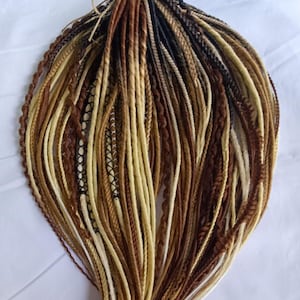 May include: A collection of synthetic hair extensions featuring a mix of blonde, light brown, dark brown, and black strands. The set includes various textures such as smooth dreadlocks, twisted braids, and thin plaits with decorative thread wraps.