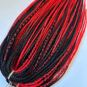 May include: A set of synthetic hair extensions featuring a mix of vibrant red and solid black dreadlocks and braids. The strands are bundled together with a thin twine at the base, showcasing various textures including smooth locks and intricate cross-stitched wraps.