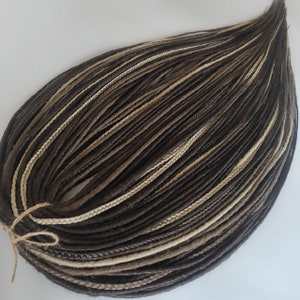 May include: A bundle of brown, light brown, and beige synthetic dreadlocks. The dreadlocks are tied together with a brown string.