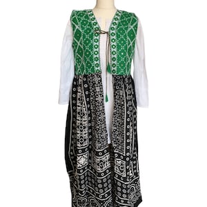 May include: A long black and white patterned skirt with a green embroidered vest. The vest has a tie closure and a tassel.