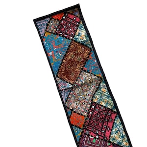 Puede incluir: Un camino de mesa largo y estrecho de patchwork con un borde negro. El camino de mesa está hecho de varias telas coloridas, incluyendo rojo, rosa, azul, verde y marrón. Las telas están cosidas juntas en un patrón de diamante, y el camino de mesa está decorado con pequeños espejos redondos.