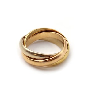 May include: A tri-color ring composed of three interlocking bands in yellow, rose, and white gold. The smooth, polished metal bands are intertwined to form a single circular structure, showcasing distinct metallic hues in a continuous loop design.
