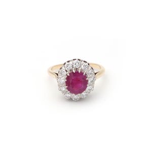 Könnte beinhalten: Ein goldener Ring mit einem ovalen Rubin als Mittelstein, umgeben von einem Kranz aus kleinen, runden Diamanten. Das Ringband ist aus schlichtem Gold. Der Rubin hat eine tiefe rote Farbe, und die Diamanten funkeln. Ein klassisches Design.