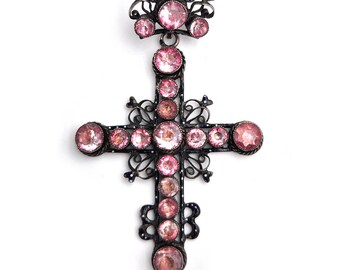 May include: A silver filigree cross pendant with pink glass stones. The cross is ornate and detailed, with a delicate design.