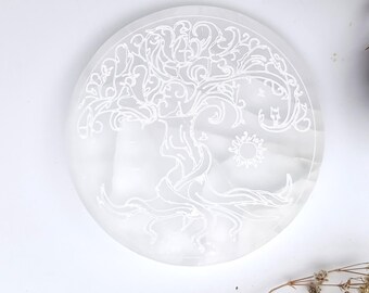 Peut inclure: Une plaque de charge en sélénite blanche et ronde, ornée d'un motif gravé d'arbre de vie. Le motif comprend des branches, des racines et un soleil. Cet objet est spirituel et décoratif.