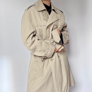 May include: A beige trench coat with a double breasted closure, a belt, and brown leather accents.