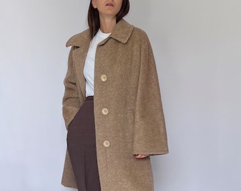 May include: A brown long-sleeved coat with a collar and button closure. The coat is worn over a white t-shirt and brown pants.