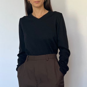 May include: A black long-sleeved v-neck jumper paired with brown high-waisted trousers.