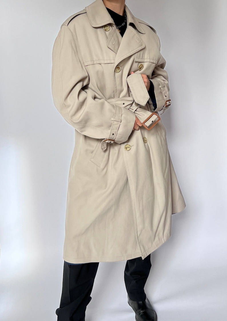 May include: A beige trench coat with a double breasted closure, a belt, and brown leather accents.