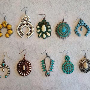 Puede incluir: Una colección de doce pares de pendientes con diversos diseños. Los pendientes presentan piedras turquesas, blancas y amarillas, junto con detalles metálicos. Estilos incluyen formas de lágrima, aro y circulares, algunos con plumas o flecos.