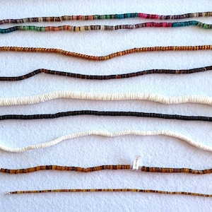Pode incluir: Uma variedade de colares de contas em várias cores e estilos. Os colares incluem fios de contas castanhas, pretas, brancas e multicoloridas. As contas parecem pequenas e uniformes, criando um design delicado. Os colares estão dispostos sobre uma superfície branca.