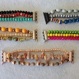 May include: Five different beaded Apple Watch bands. The bands are made with various colours and styles of beads, including turquoise, yellow, red, green, and brown.