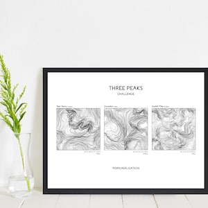 May include: Black framed print featuring the text "THREE PEAKS CHALLENGE" above three contour maps of Ben Nevis, Snowdon, and Scafell Pike. The word "PERSONALISATION" is below the maps.