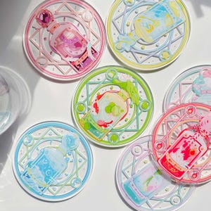 May include: Set of 6 colorful round coasters with a whimsical design featuring glass bottles with different liquids and magical symbols. Each coaster has a unique color scheme and design.