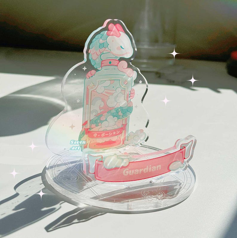 May include: A clear acrylic stand featuring a pink and blue cartoon character holding a bottle. The bottle has a pink and blue label with Japanese text that reads "守護ーGuardian". The stand has a pink banner that reads "Guardian".