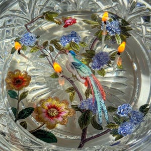 May include: A clear glass bowl with a floral design and a blue bird. The bowl is filled with water and has four lit candles floating in it.