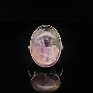 May include: A silver ring with a large oval-shaped amethyst gemstone. The amethyst is a light purple color with a hint of pink and white.