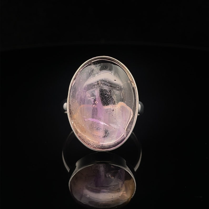 May include: A silver ring with a large oval-shaped amethyst gemstone. The amethyst is a light purple color with a hint of pink and white.