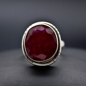 May include: A silver ring with a large, faceted ruby gemstone. The ruby is a deep red color and has a high polish.