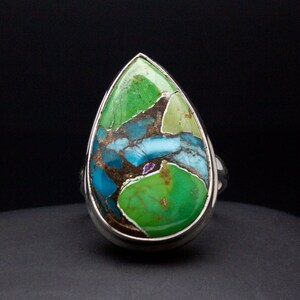Peut inclure: Une bague en forme de larme avec une pierre précieuse multicolore sertie dans de l'argent. La pierre précieuse est un mélange de vert, de bleu et de brun.