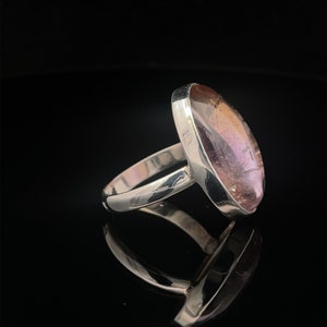 May include: A silver ring with a large oval-shaped amethyst gemstone. The gemstone is a light purple color with a hint of pink.