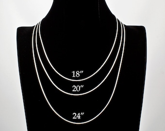 May include: Three silver chains of different lengths, 18 inches, 20 inches, and 24 inches, displayed on a black mannequin.
