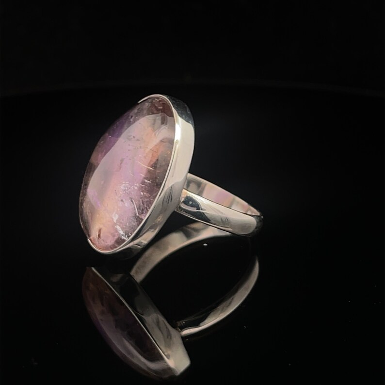 May include: A silver ring with a large oval amethyst gemstone. The gemstone is a deep purple color with hints of pink and white.
