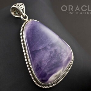 Puede incluir: Un colgante de plata con una piedra grande de fluorita p&uacute;rpura y blanca. El colgante tiene un dise&ntilde;o detallado y adornado alrededor de la piedra.