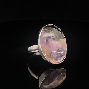 May include: A silver ring with a large oval-shaped amethyst gemstone. The gemstone is a light purple color with hints of pink and yellow.
