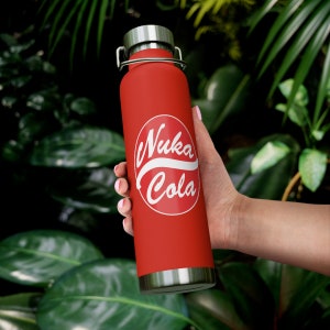 May include: Red stainless steel water bottle with a white Nuka Cola logo. The bottle is being held by a hand.