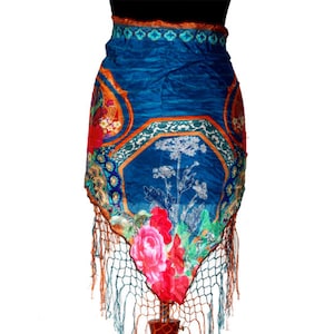 Puede incluir: Una falda de seda azul con estampado floral y ribete de flecos. La falda se muestra en un maniquí de madera.