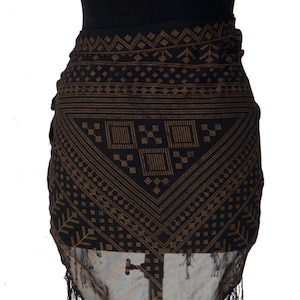 Puede incluir: Una falda de envoltura negra y dorada con flecos. La falda está hecha de una tela transparente y tiene un diseño geométrico.