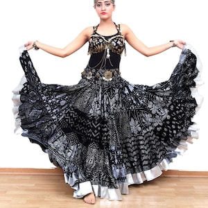 Puede incluir: Una mujer con un traje de danza del vientre negro y plateado con un tocado plateado. La falda es una falda circular con un ribete plateado y un patrón negro y plateado.