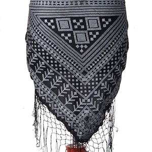 Puede incluir: Bufanda negra y blanca con estampado geométrico y flecos. La bufanda está atada alrededor de la cintura de un maniquí.