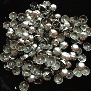May include: A large pile of silver-toned metal dome-shaped buttons. The buttons have a raised centre and a flat back with a small hole in the centre.