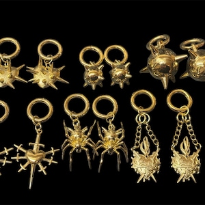 May include: A set of 10 gold-toned body jewelry pieces. The jewelry features a variety of designs, including spikes, hearts, spiders, and swords. The jewelry is designed for use as ear or body piercings.