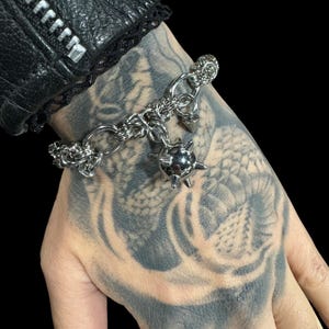 May include: A silver chain bracelet with a spiked ball charm. The bracelet is made of interlocking metal rings and has a simple, edgy design.