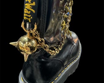 May include: Black leather platform boots with a gold chain and a spiked ball attached to the ankle. The boots have yellow stitching and a yellow "Dr. Martens" label on the back.