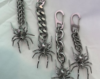 May include: Four silver keychains with a spider charm. Each keychain has a different style of chain and a silver carabiner clip.