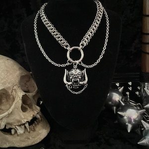 May include: A silver chain necklace with a large silver pendant featuring a snarling animal head with horns. The pendant is attached to a large silver ring.