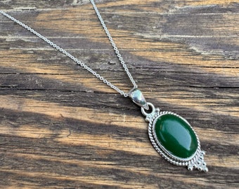 May include: A silver chain necklace with a green oval pendant. The pendant has a silver border with a decorative design.