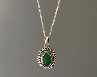 May include: A silver chain necklace with a green oval gemstone pendant. The pendant is surrounded by a silver beaded border.