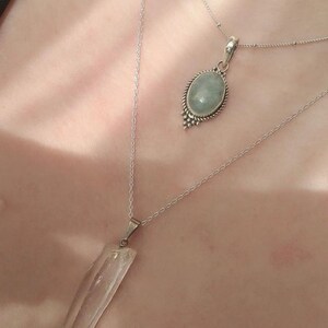 Op de afbeelding: Twee zilveren kettingen met kristallen hangers. De ene hanger is een heldere kwartskristal, de andere is een lichtblauwe aquamarijnkristal.