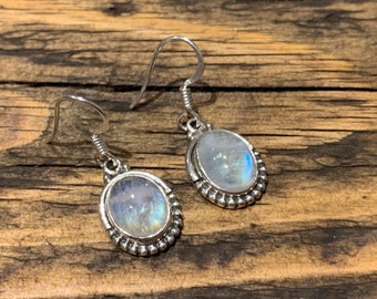May include: A pair of silver dangle earrings with oval moonstone gemstones. The earrings have a beaded border around the stones.