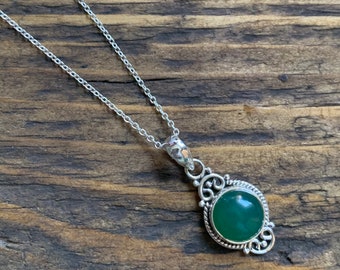 May include: A silver chain necklace with a green gemstone pendant. The pendant is set in a silver filigree design.